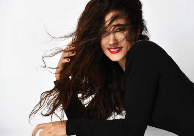 Uzun kıvırcık esmer saçlı, siyah şık elbiseli, gülümseyen genç bir kadın dirseklerinin üzerinde yerde yatıyor.