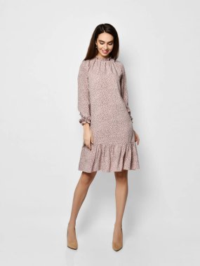 Genç ve güzel bir kadın yeni moda poz veriyor. Uzun, sade, pembe renkli bir elbise. Beyaz üzerinde mutlu bir gülümseme.