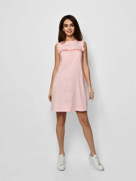 Ung vacker kvinna poserar i nytt mode lång casual pastell rosa färg klänning glad leende promenader på vitt — Stockfoto