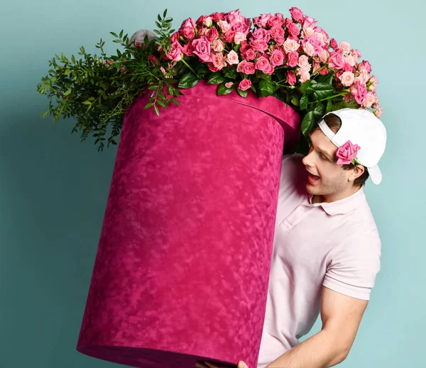 Portrait of athletic surprised man delivery guy holding huge valentines day pink box with flowers roses looking at it