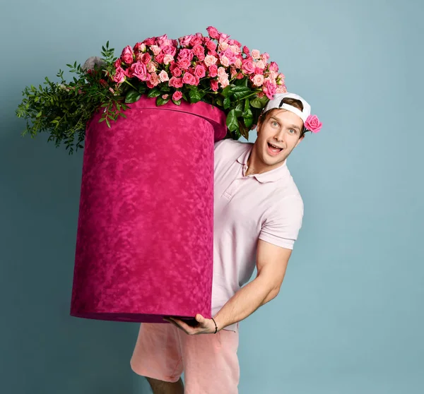 Portrait of athletic happy smiling surprised man delivery guy holding huge valentines day pink box with flowers roses