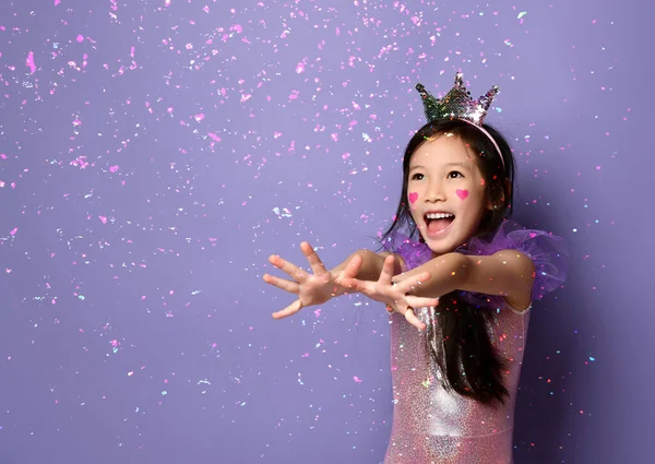 Gülen Asyalı küçük kız. Parti elbisesi ve tacı giymiş prenses. Ellerini kar tanelerine uzatıyor. — Stok fotoğraf