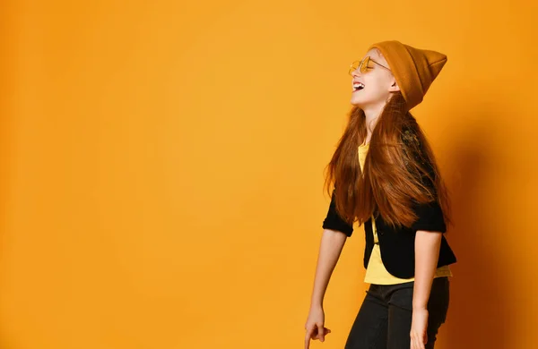 Рудоволоса дівчина в стильних сонцезахисних окулярах капелюх жовта футболка і чорна куртка сміється голосно тролінг знущання — стокове фото