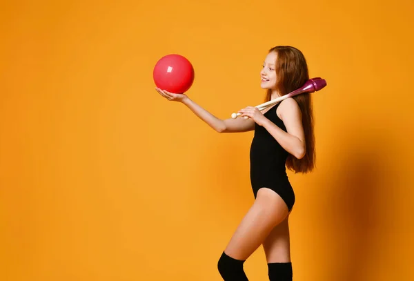 Рыжая девочка-гимнастка в купальнике смотрит на розовый мяч, который она держит на открытой ладони. — стоковое фото