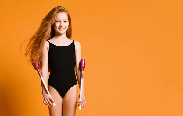 Uśmiechnięta rudowłosa nastolatka gimnastyczka w stroju kąpielowym pozuje z gimnastycznymi macami na tle z wolną przestrzenią do kopiowania — Zdjęcie stockowe