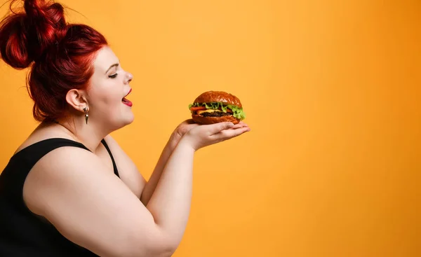 Happy overweight fat woman happy hold burger cheeseburger sandwich with beef in hand on yellow. — Foto de Stock