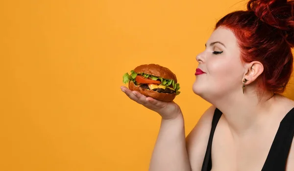 Happy overgewicht dikke vrouw gelukkig hold hamburger cheeseburger sandwich met rundvlees in de hand op geel — Stockfoto