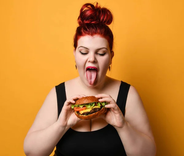 Happy overweight fat woman happy hold burger cheeseburger sandwich with beef in hand on yellow