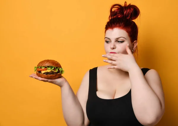 Glücklich übergewichtige dicke Frau glücklich halten Burger Cheeseburger Sandwich mit Rindfleisch in der Hand auf gelb — Stockfoto