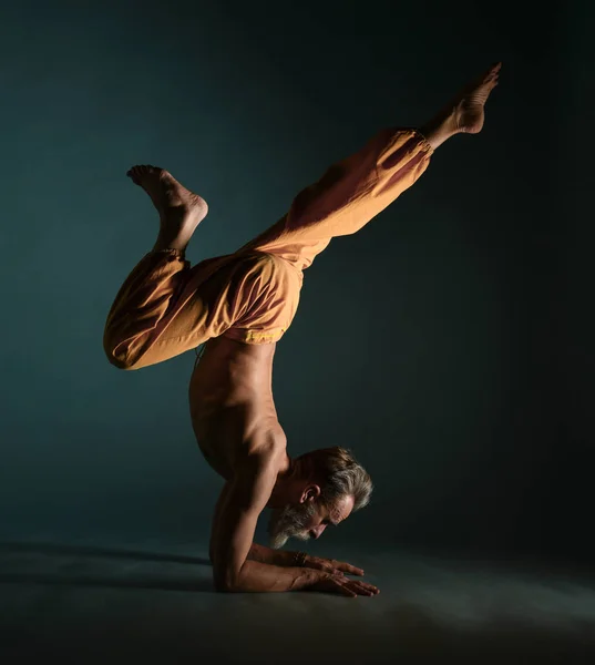 Le vieil homme à la barbe grise faisant du yoga, des pilates, de l'entraînement physique, des exercices d "étirement, de l'asana ou de l" équilibre au sol — Photo