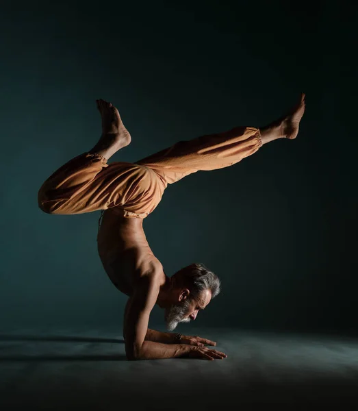 Le vieil homme à la barbe grise faisant du yoga, des pilates, de l'entraînement physique, des exercices d "étirement, de l'asana ou de l" équilibre au sol — Photo