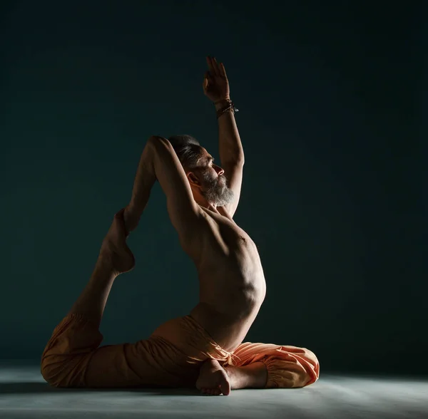 Le vieil homme à la barbe grise faisant du yoga, des pilates, de l'entraînement physique, des exercices d "étirement, de l'asana ou de l" équilibre au sol — Photo