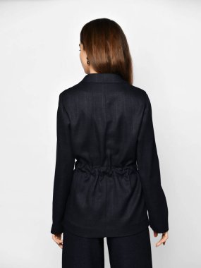 Şık takım elbiseli güzel esmer kadın gri arka planda ters poz veriyor.