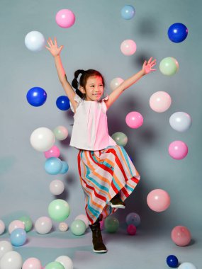 Şık çizgili Maxi etekli mutlu Asyalı kız eğlenceli zıplamalar renkli hava balonlarıyla çevrili danslar atlamalar