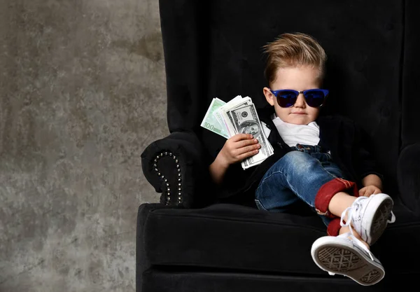 Ernstige arrogante rijke jongen jongen miljonair zit met een bundel geld dollars contant in grote luxe fauteuil — Stockfoto