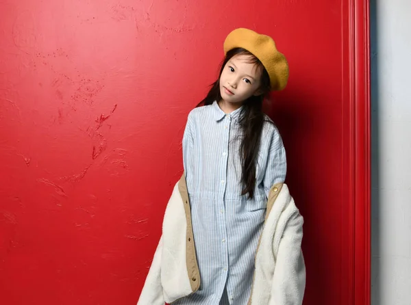 Bonito lindo asiático niño chica iblue camisón fieltro boina y beige chaqueta es posando sobre rojo —  Fotos de Stock