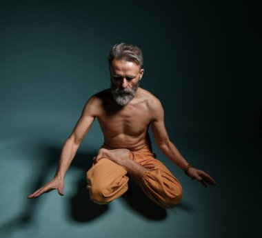 Gri sakallı yaşlı adam yoga yapıyor, pilates yapıyor, spor yapıyor, esneme egzersizleri yapıyor, asana havada duruyor ya da yerde denge çalışması yapıyor.