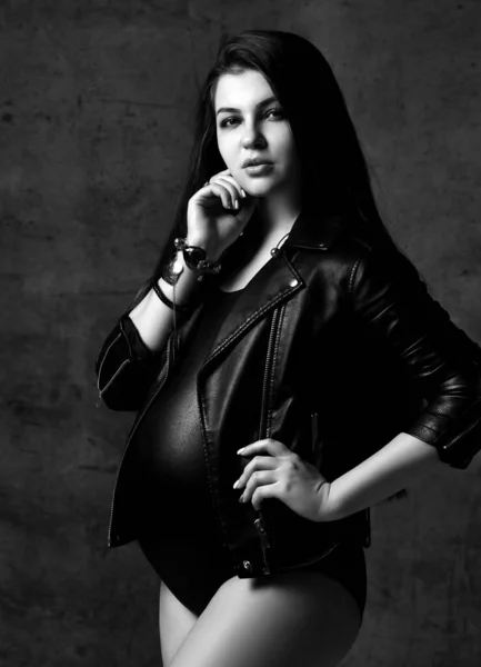 Mladá krásná štíhlá těhotná žena s dlouhými vlasy v černém těle a koženou bundou. Těhotenství módní vzhled koncept — Stock fotografie