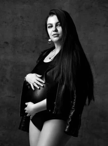 Jovem bela mulher grávida magra com cabelos longos em corpo preto e jaqueta de couro. Gravidez moda olhar conceito — Fotografia de Stock