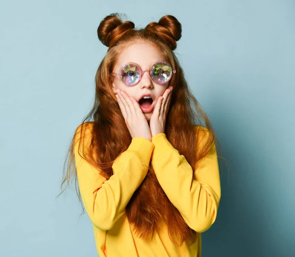 Surpris jeune fille aux cheveux roux dans des lunettes rondes de mode et sweat-shirt jaune halètements couvrant ses joues avec les mains — Photo