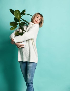 Beyaz kazaklı sarışın manken elinde yeşil tropikal bitkiler olan yeni bir daireye taşınacak.