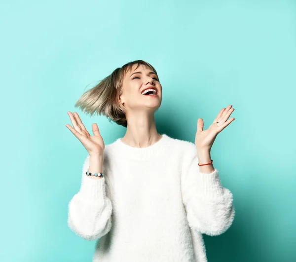 Menina loira encantadora em camisola branca sorrindo gritando rindo dançando com levantar as mãos para cima, posando em azul pastel — Fotografia de Stock