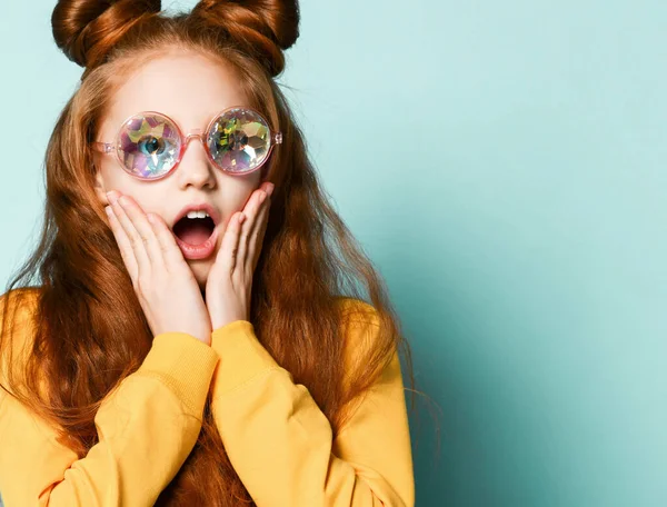 Surpreendida menina adolescente ruiva na moda óculos redondos e suspiros de camisola amarela cobrindo suas bochechas com as mãos — Fotografia de Stock