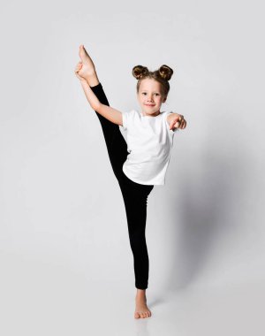 Çocuk evde jimnastik egzersizleri yapıyor. Bacağı elinde ve diğer eliyle bizi işaret ediyor.