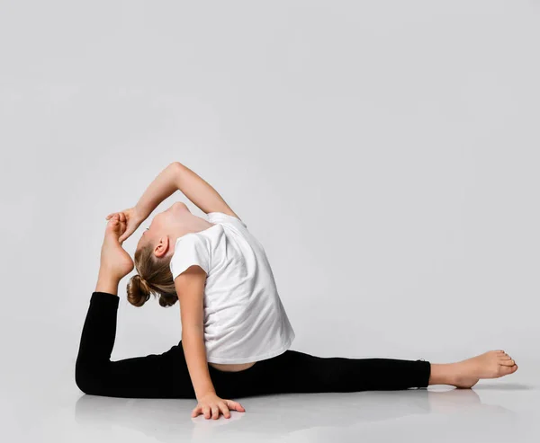 Niña está haciendo ejercicios de gimnasia en casa en las divisiones de estudio con una pierna hacia arriba cuerpo doblado y la cabeza lanzada de nuevo a los pies — Foto de Stock