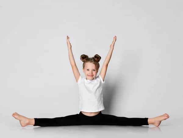 Sonriente niña hace ejercicios de gimnasia en casa se divide con las manos extendidas —  Fotos de Stock