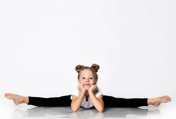 Sonriente niña hace ejercicios de gimnasia en casa se divide doblar hacia adelante con la cabeza inclinando sus manos —  Fotos de Stock