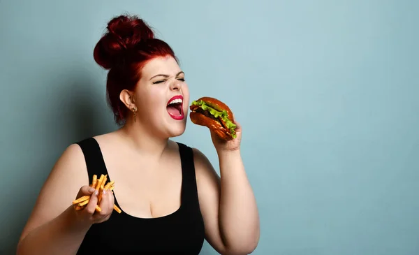 Feliz excesso de peso mulher gorda feliz segurar hambúrguer cheeseburger sanduíche com carne bovina e batatas fritas na mão — Fotografia de Stock