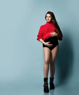 Kırmızı kazaklı güzel hamile kız karnında hamilelik, annelik, insanlar ve beklenti konseptini taşıyor.