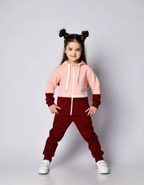 Healthy active brunette kid girl with buns in modern stylish pink brown sportswear stands with her legs wide apart