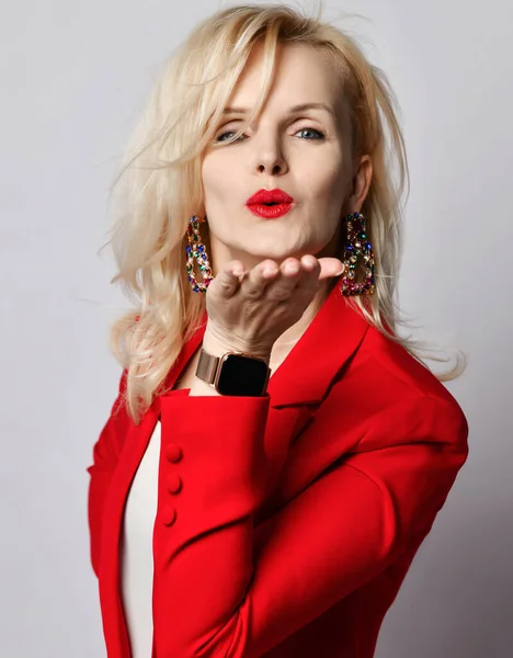 Портрет молодой красивой блондинки, улыбающейся женщине в стильном элегантном темно-красном официальном костюме и массивных серьгах, дующих поцелуем — стоковое фото