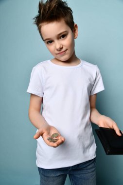 Modern saç stili, şık giyinen, ayakta duran ve elinde siyah çantadan birkaç bozuk para gösteren küçük sevimli bir çocuk.