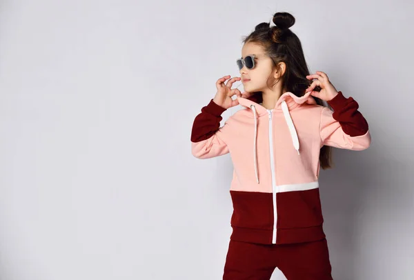 Cooles brünettes Mädchen in rosa braunem Kapuzenpulli und Sonnenbrille steht mit Kapuze ihres Kapuzenpullis und schaut in den Kopierraum — Stockfoto