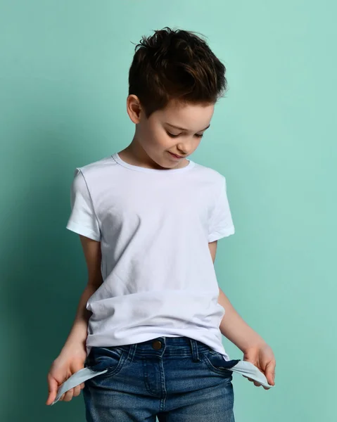 Kleine schattige jongen met modern kapsel in stijlvolle casual kleding staan en tonen lege zakken zonder geld concept — Stockfoto