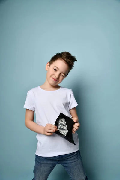 Pequeno menino bonito com penteado moderno em t-shirt branca mostrando cem dólares em dinheiro em carteira bolsa preta — Fotografia de Stock