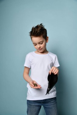 Beyaz tişörtlü çocuk pastel mavi arka planda boş cüzdan ve bozuk para gösteriyor. Konut için ödenecek bir şey yok Para kavramı yok