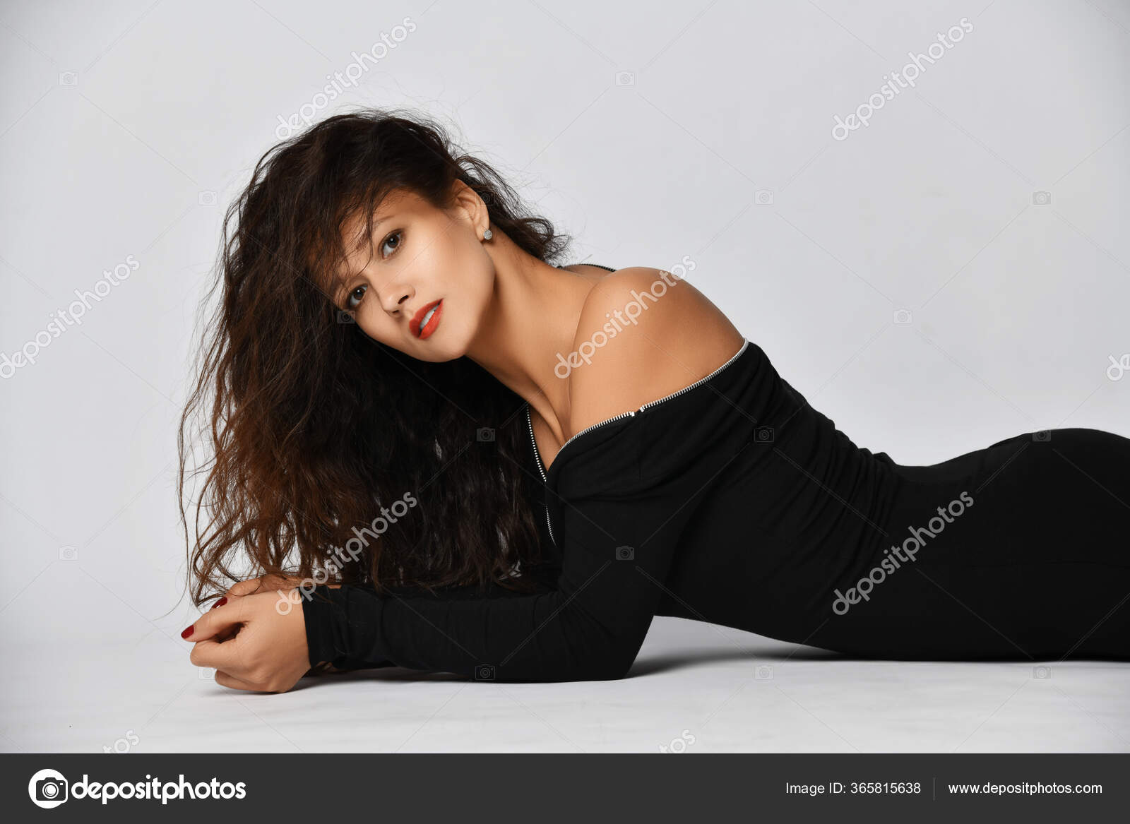 Portrait of woman with long curly brunette hair in black tight off-shoulder dress lies sexual posing on the floor Stock Photo by ©dml5050 365815638 picture