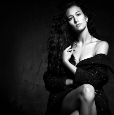 Çapraz bacaklı, çıplak bedenin üzerinde yün ceketli, şehvetli asil bir kadının siyah beyaz portresi.