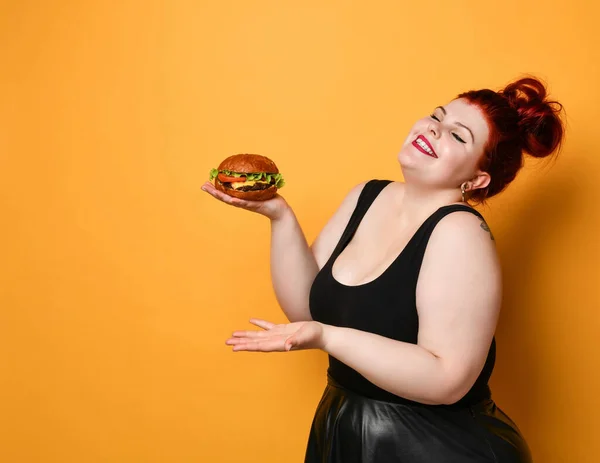 Happy overweight fat woman happy hold big burger cheeseburger sandwich with beef in hand laughing on yellow