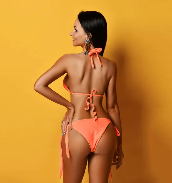 Junge schöne lächelnde, braun gebrannte, brünette Frau im sexy orangefarbenen Bikini, die rückwärts steht — Stockfoto