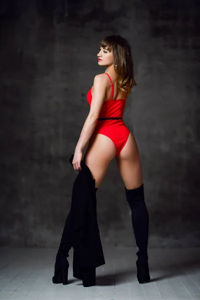 Ung vacker smal brunett kvinna i sexig röd baddräkt eller underkläder och svarta höga stövlar står bakåt — Stockfoto