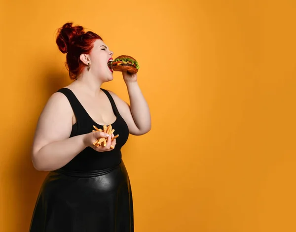 Plus-size dikke vrouw met overgewicht neemt een lange hebzuchtige hap van hamburger cheeseburger sandwich met rundvlees op geel — Stockfoto