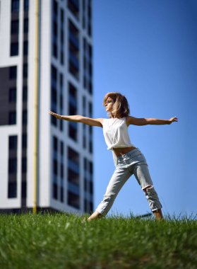 Şehir merkezindeki şehir parkında yoga germe egzersizleri yapan genç bir kadın.