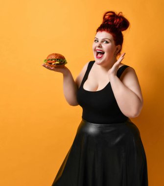 Şişman, mutlu bir kadın açık avucunda tuttuğu biftekli burger sandviçine bakar.