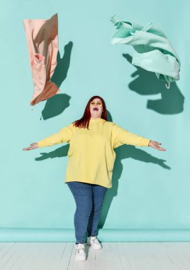 Genç, mutlu, kızıl saçlı, kilolu, sıradan giyimli ve spor ayakkabılı bir kadın. Uçan mavi ve pembe kapüşonluyla oynuyor.