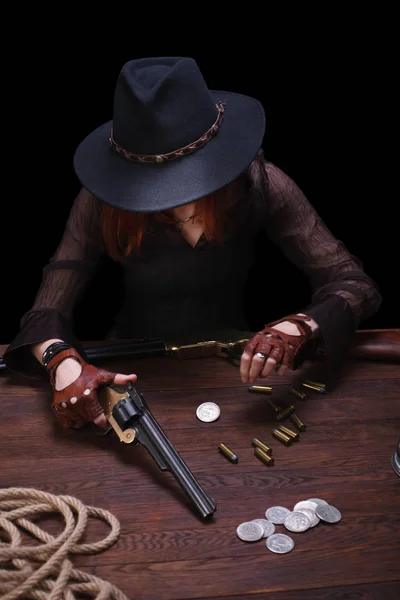 wild west girl with revolver gun sitting at the table with ammunition and silver coins